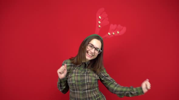 A Young Woman Is Dancing with a Headband in the Form of Christmas Antlers. Studio Shooting on a Red