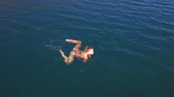 Aerial view. A beautiful woman with a slim figure in a swimsuit swims breaststroke in water sea