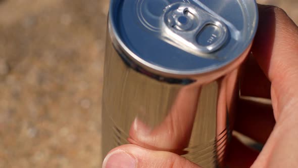 A woman's hand opens an iron can, the can opens and a drink is poured out.