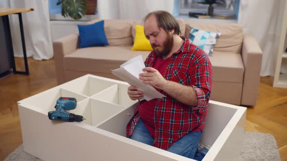 Young Overweight Man Installing New Furniture Using Selfassembly Kit Indoors