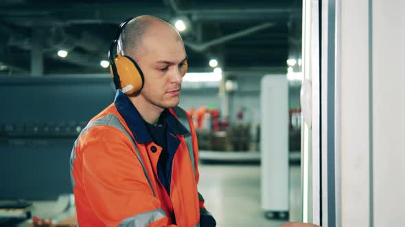 Bald Male Engineer Operates a Machine at a Factory Using a Touchscreen