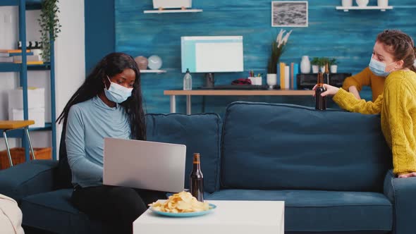 Woman Holding Beer Bottle Looking at Laptop Discussing with Friend