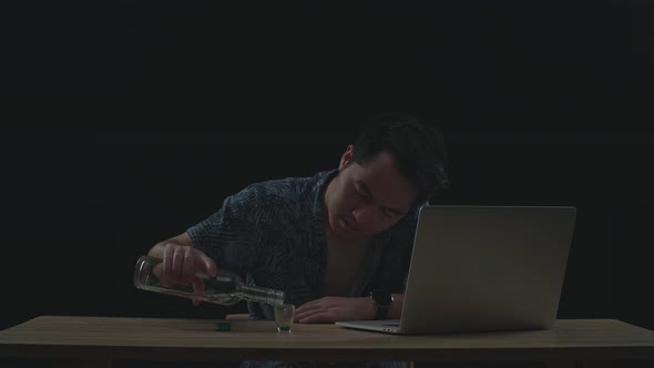 Asian Man Drinking Vodka While Working On A Laptop In Black Background