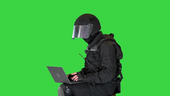 Riot Police Officer Sitting and Using Laptop on a Green Screen Chroma Key