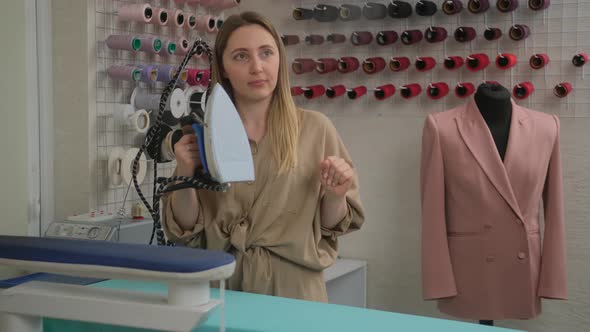 A fashion tailor designer at work hovering clothes with an iron and steam in a sewing workshop