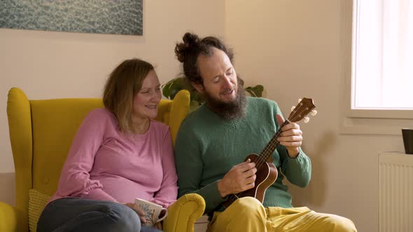 Man playing the ukulele to pregnant wife at the living room.
