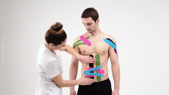 Female therapist applying kinesiology tape on a man's abdomen on the light background