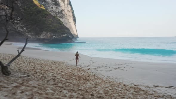 Female Tourist in Swimsuit Running Barefoot in Sand Towards Beautiful Beach