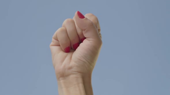 Close-up of Female Fist Raising Up at the Background of Clear Blue Sky. Unrecognizable Woman Showing