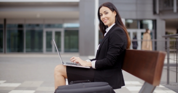 Woman Looking Over With Laptop On Bench alt