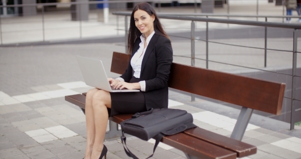 Woman Looking Over With Laptop On Bench alt