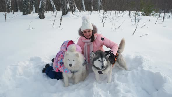 Woman with Daughter Embracing Sled Dogs on Snow