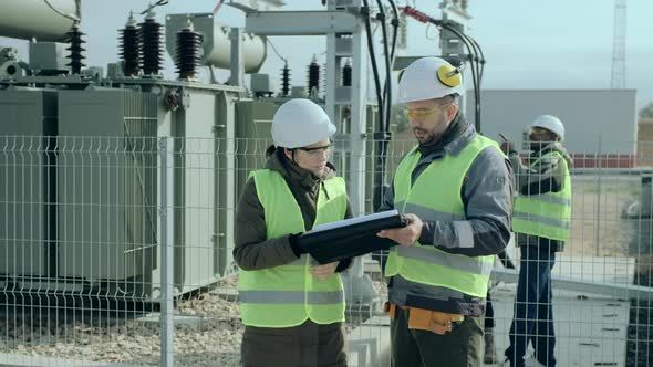 Power Engineers Man and Lady in Helmets Discuss Project