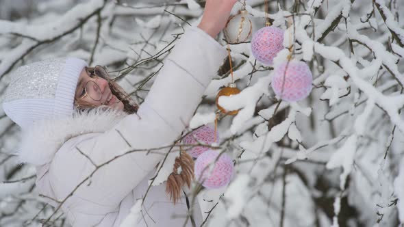 A Girl Hangs Christmas Toys on Trees in a Snowy Forest