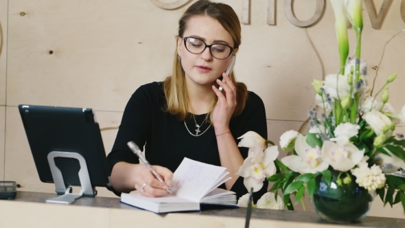 Young Woman Speaks On Phone, Taking Notes On a Pad