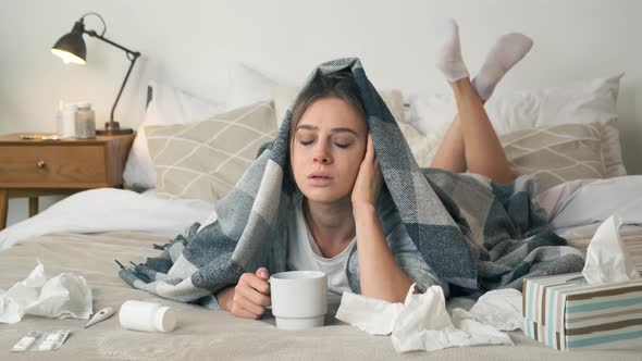 Sick Woman Covered with Blanket Holding Cup of Tea Lying on Bed at Home