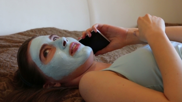 Girl With Cosmetic Mask On Her Face Talking On The Smartphone