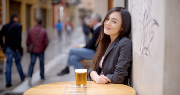 Friendly Young Woman Sitting Enjoying a Beer alt