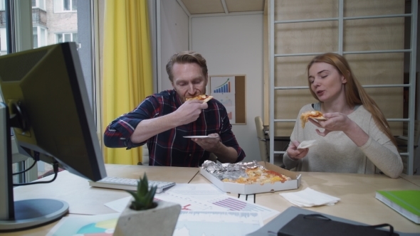 Man And Woman Eating Pizza At Workplace