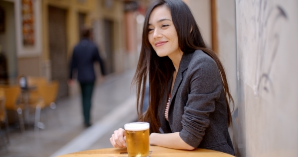 Friendly Young Woman Sitting Enjoying a Beer alt
