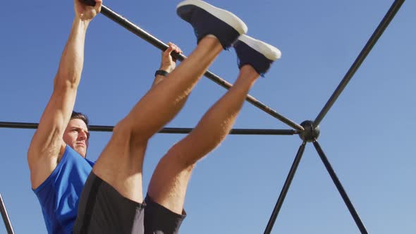 Fit caucasian man exercising outside, doing leg raises on a climbing frame