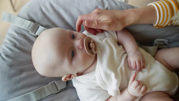 Mom Putting Pacifier on Cute Little Baby on a Rocker and Holds Its Tiny Hand