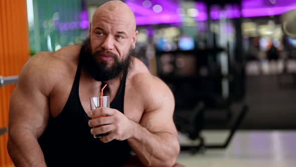 A Sporty Man with a Juice Cocktail Relaxes Enjoying a Morning Breakfast After a Workout Sitting on a