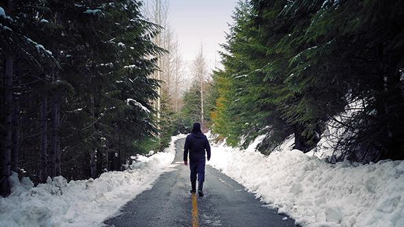 Man Walks Down Snowy Road In Woods