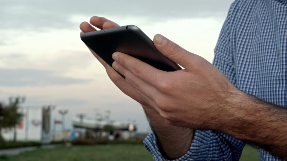 Man Clicks On a Digital Tablet At Sunset