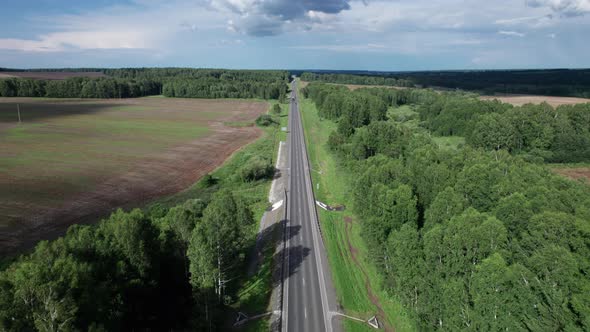 Aerial View of Scenic Road Between Green Trees with Pines on a Sunny Summer Morning