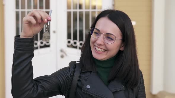 A happy woman and owner of a newly bought house shakes the key in the air.