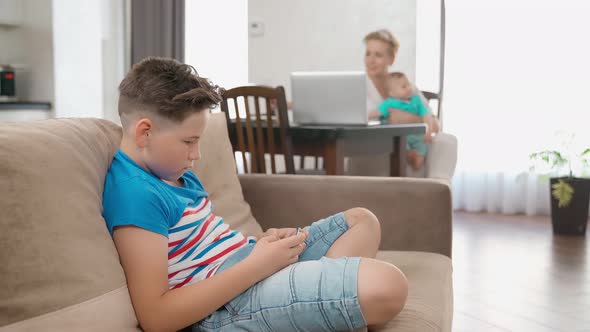 Boy Playing on Smartphone While Mother Working on Laptop