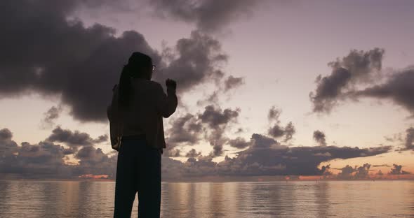 Silhouette of woman raising hand at sunrise time