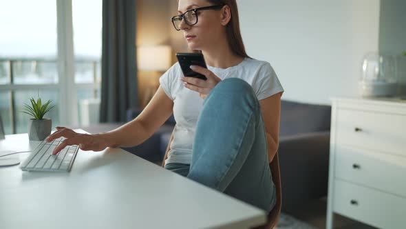 Casually Dressed Woman with Headphones Working with a Computer and Smartphone at Home in a Cozy