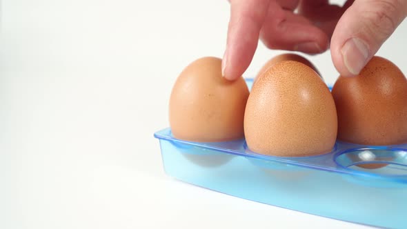 Chicken eggs in a blue plastic egg container, hand takes one brown egg 