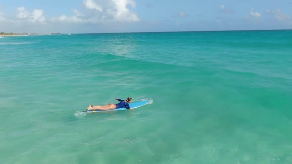 Woman is Lying on a Surfboard and Swimming in the Ocean Light Blue Water