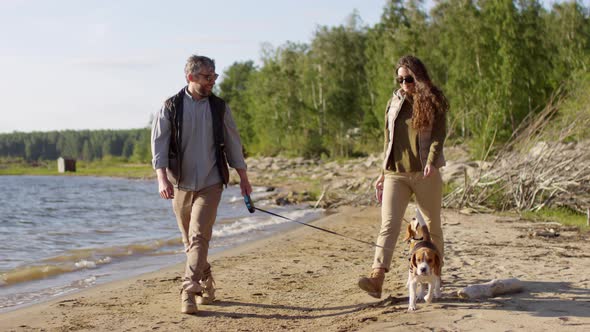 Tourist Couple Walking with Beagle Dogs along Lake Shoreline