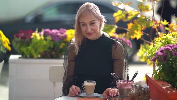 Pretty Woman Is Relaxing in Street Cafe, Drinking Cappuccino or Latte and Smiling, Sitting at Autumn