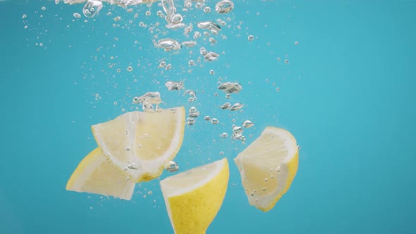 Slow Motion of Falling Lemon Slices Into Splashing Water on Blue Background