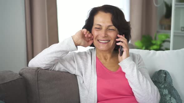 Portrait of Mature Woman Talking Phone Sitting on Sofa in Home Room