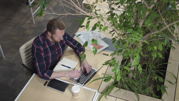 Bearded Man Working At a Computer And Making Notes. alt