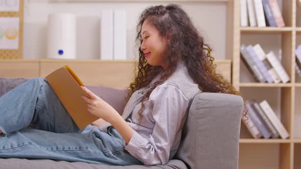 Young woman reading book while relaxing with pleasure on the couch in the living room. Concept of le