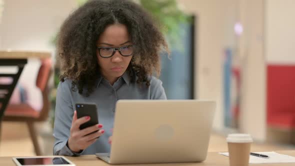 Young African Woman with Laptop Using Smartphone
