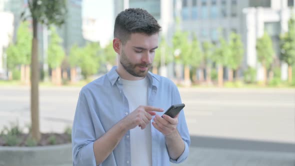 Young Man Browsing Internet on Smartphone Outdoor
