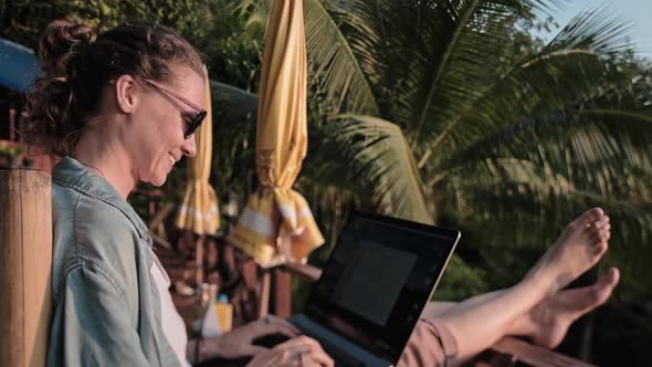 Freelancer woman sits with a laptop on a high bar chair. 