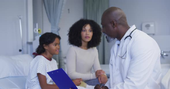 African american senior male doctor with clipboard talking to mother and daughter at hospital