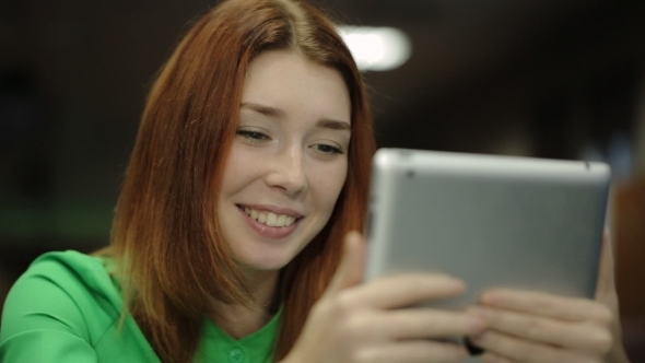 Young Woman Holding a Tablet Computer, Looking At Screen And Smiling, Saying Something.