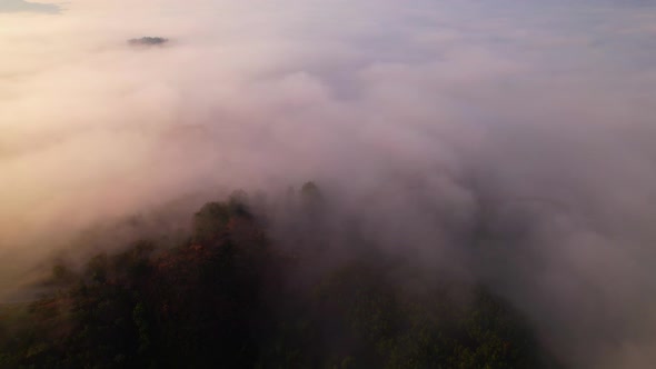 4K aerial view over mountain at sunrise in heavy fog. golden morning sunlight