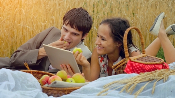  Happy Couple In Love Sitting On Picnic In Wheat Field Use Tablet And Eating Apples