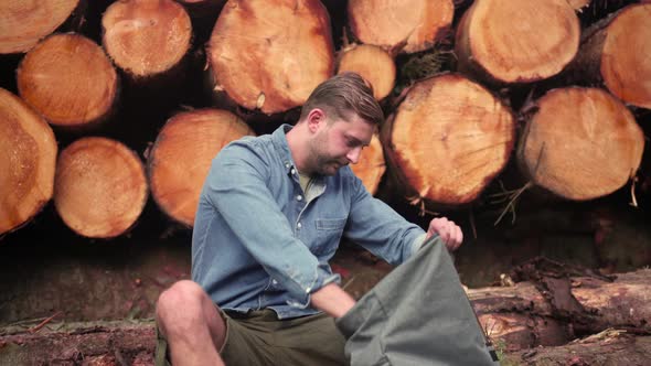 Hiker sitting on tree trunk and taking out binoculars from backpack